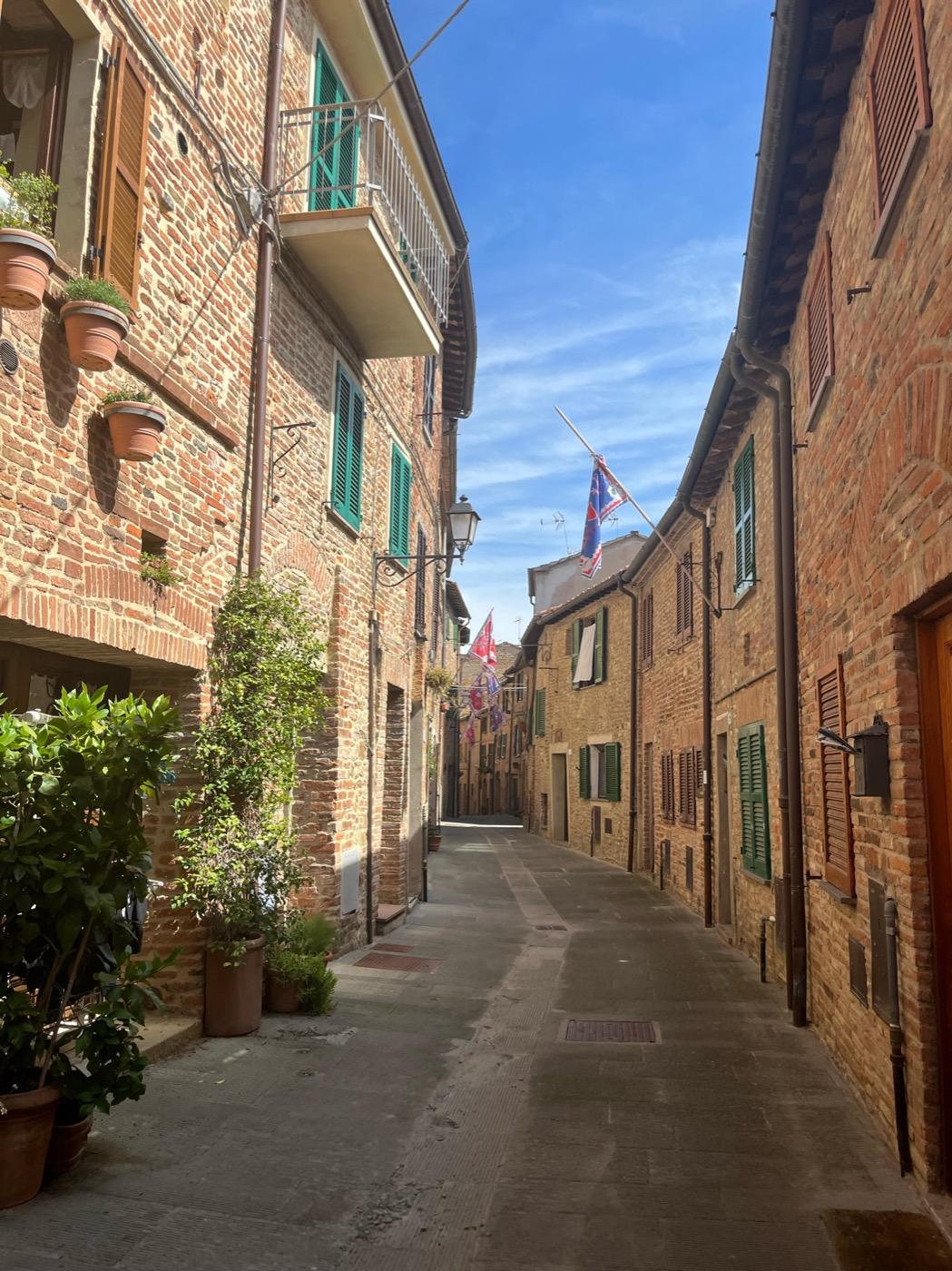 Sunlit brick alley with green shutters and festival flags in an Italian town